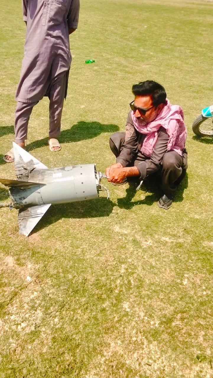 A man crouches beside the fin section and serial-numbered booster of an Indian MR-SAM interceptor recovered in a Sialkot field