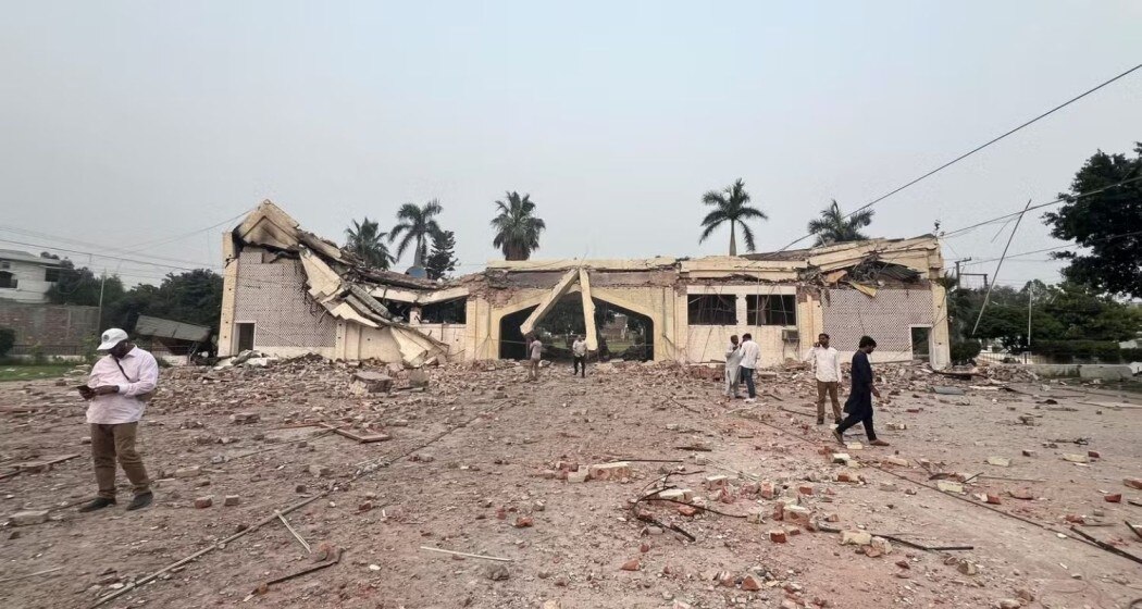 Ground-level photo of the destroyed Markaz Taiba building at Muridke, roof collapsed, rubble strewn across the courtyard